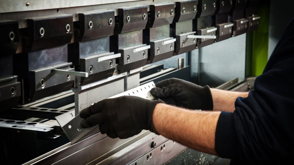 Gloved hands bending a stainless steel sheet on a press brake