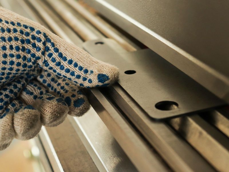 Gloved hand holding a flat metal plate with two holes against machine tooling