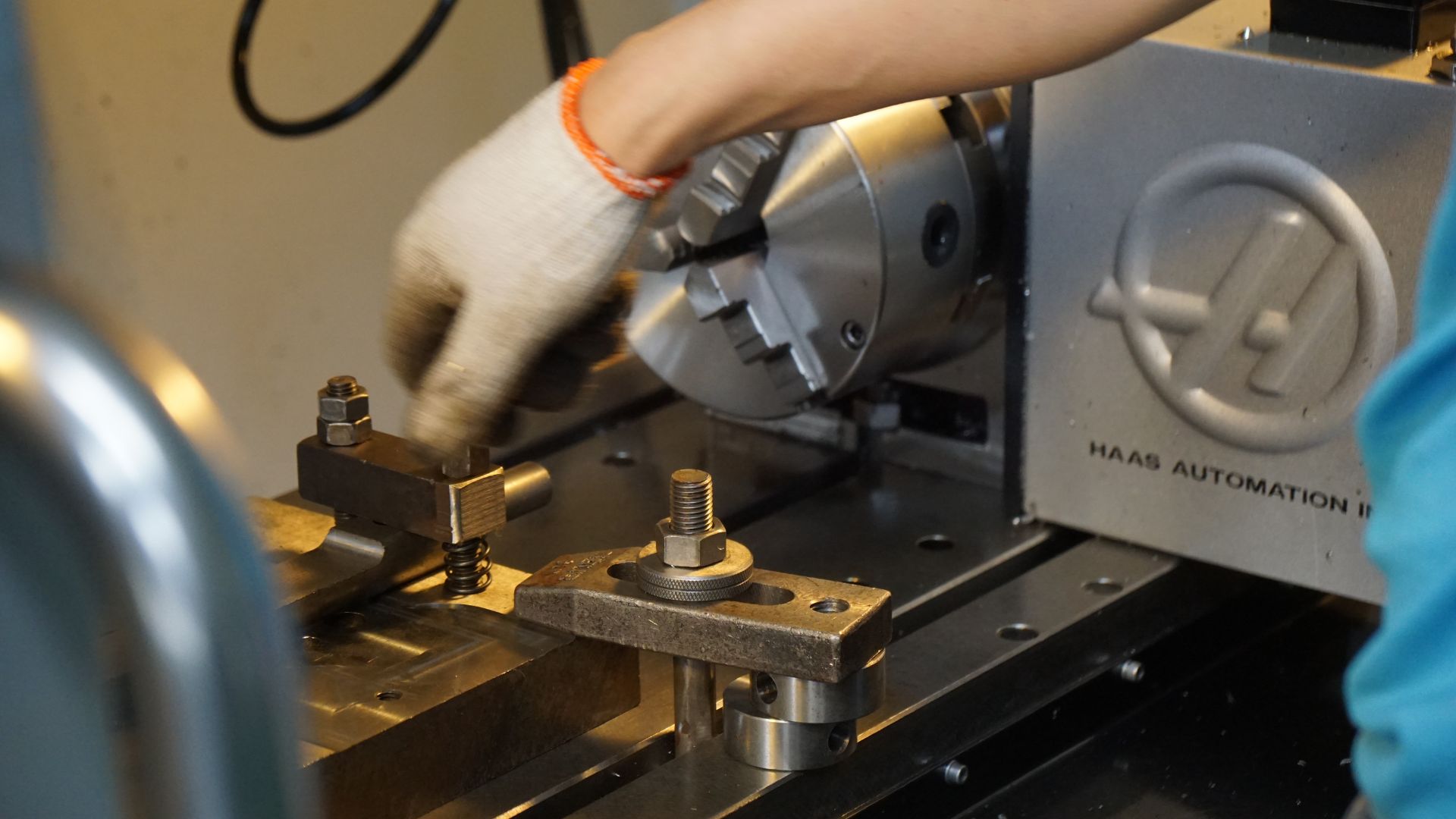 Gloved hand clamping a part on a CNC machine table beside a three-jaw chuck