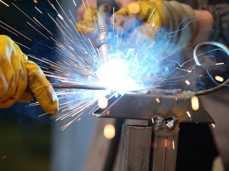 Welder in yellow gloves joining steel sections, with sparks flying