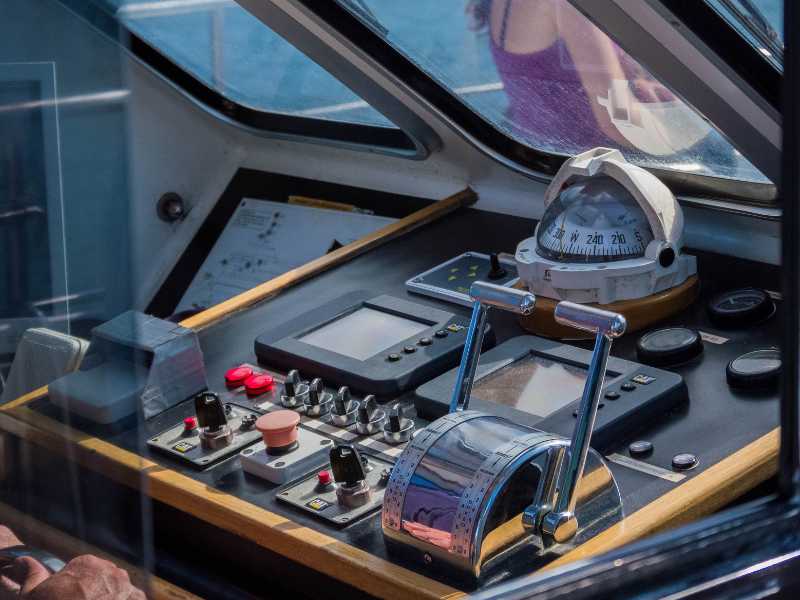 Boat cockpit control panel with throttle lever, navigation screens, and a compass in a glassed helm area