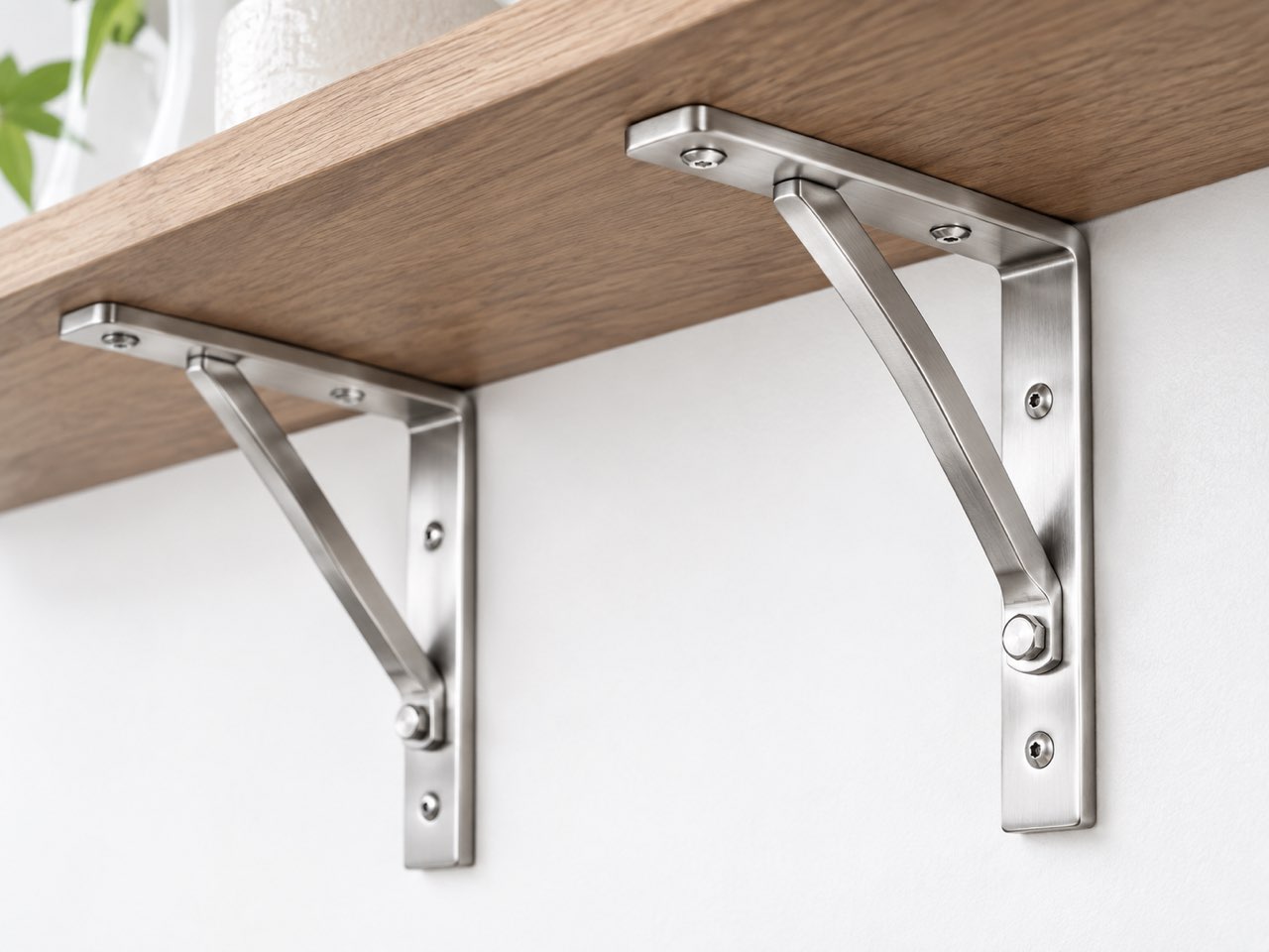 Stainless steel folding shelf brackets mounted under a wood shelf, showing arm length and diagonal support thickness