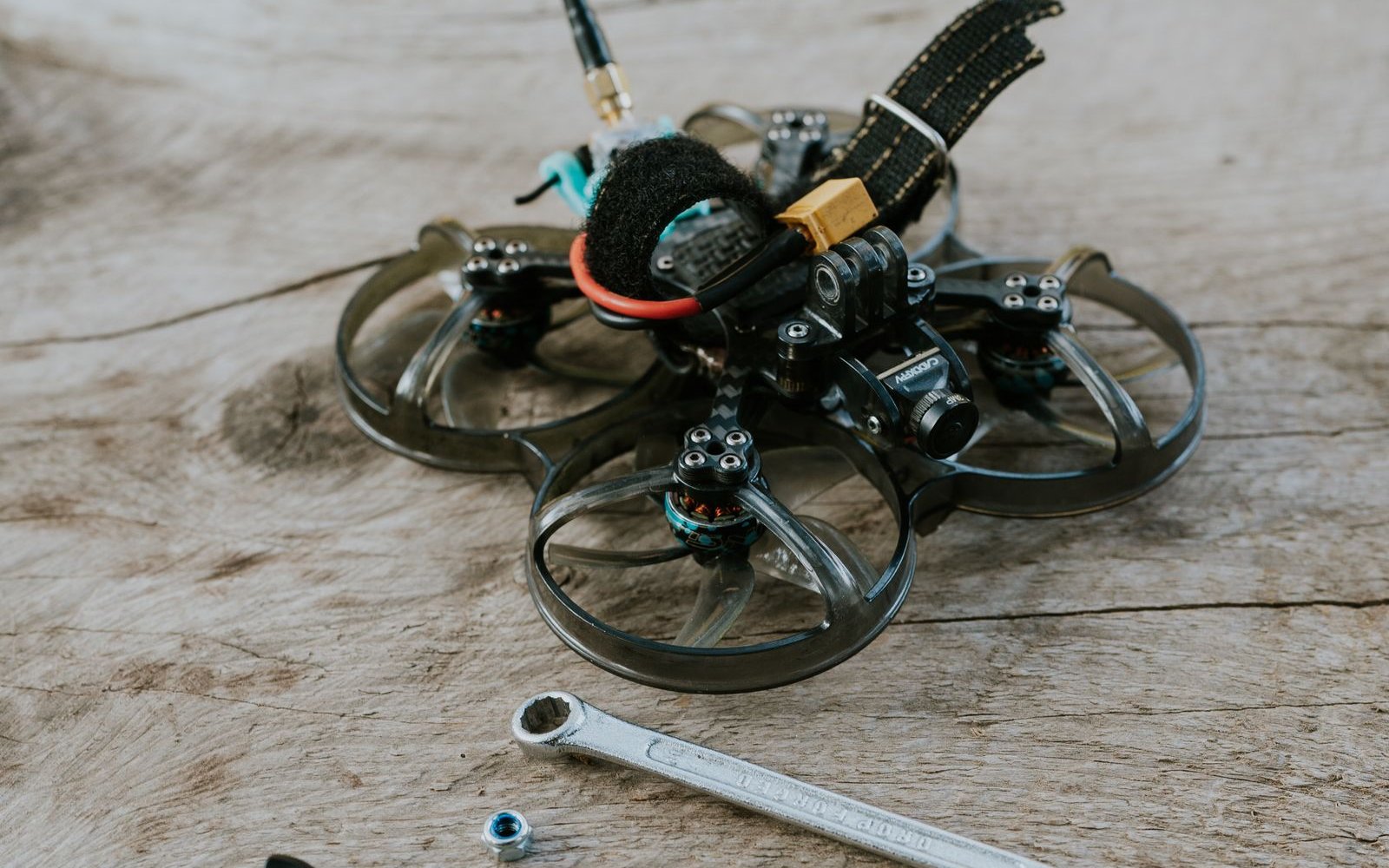 Small drone frame on a wooden bench beside a wrench