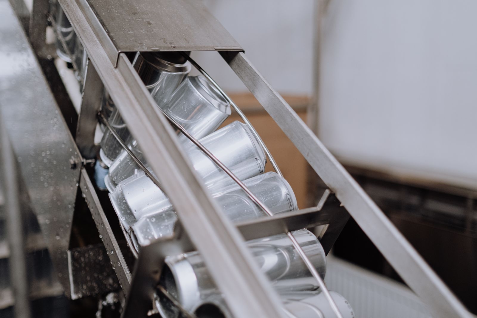 Cans moving along a stainless steel conveyor chute on a packaging line