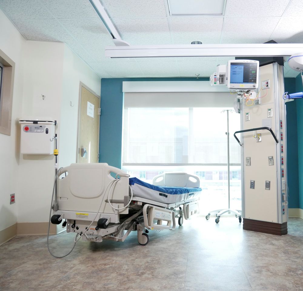 Hospital bed in an empty patient room beside a wall-mounted monitor